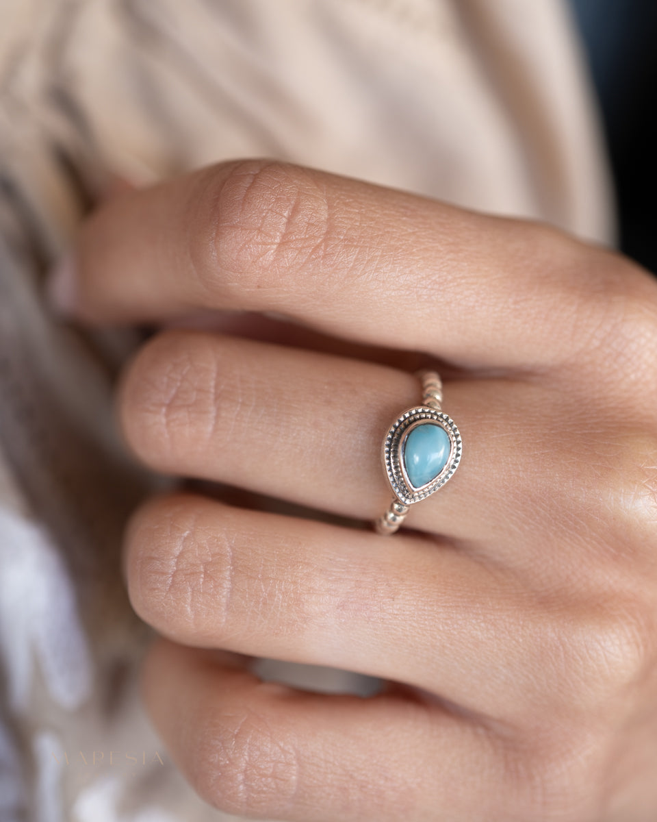 Close-up of a hand wearing a ring with a blue larimar 
gemstone.