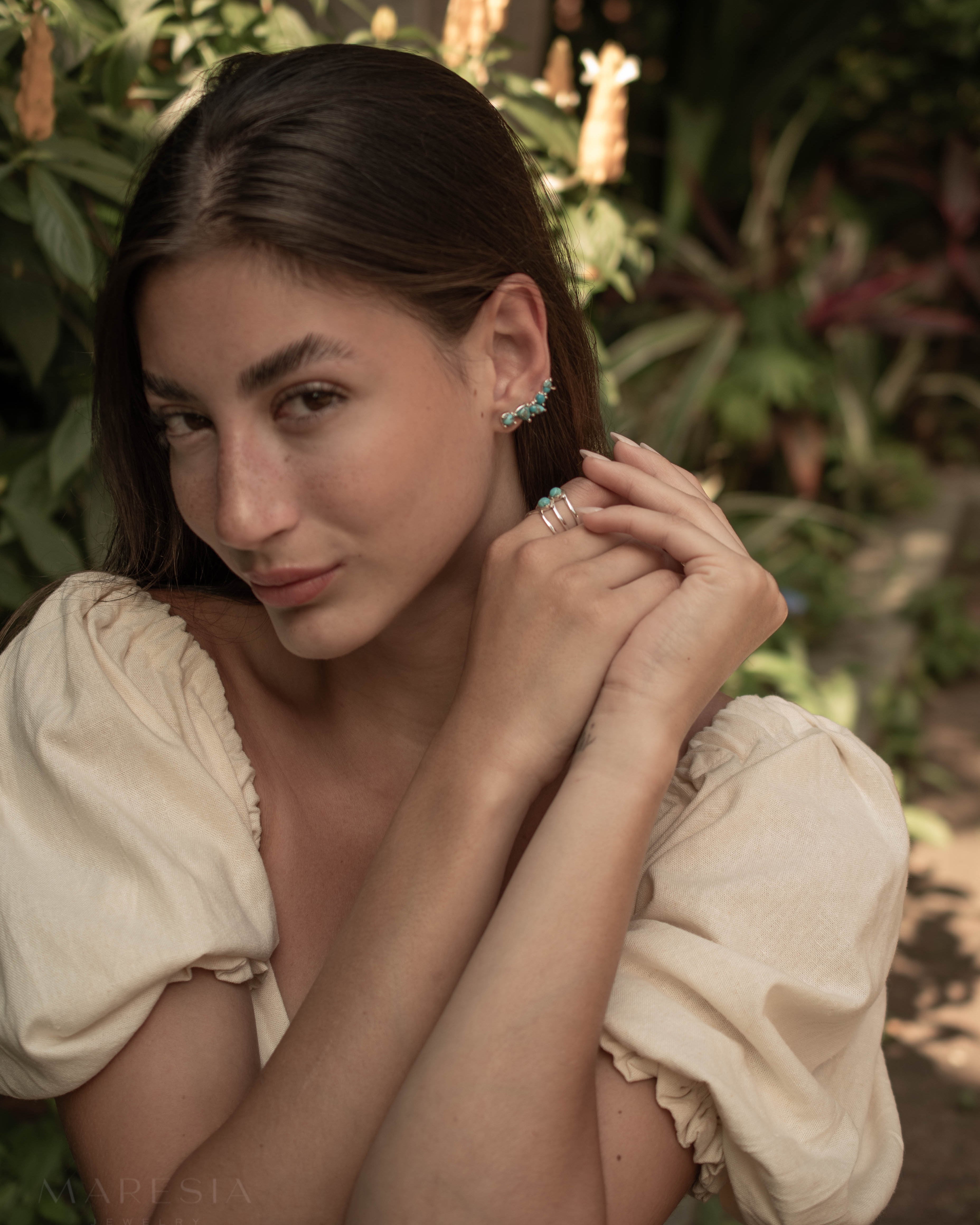Woman adjusting her turquoise climber earrings with a natural background