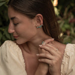 Woman wearing earrings and a ring with a blurred natural background