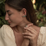 Woman wearing earrings and a ring with a blurred natural background