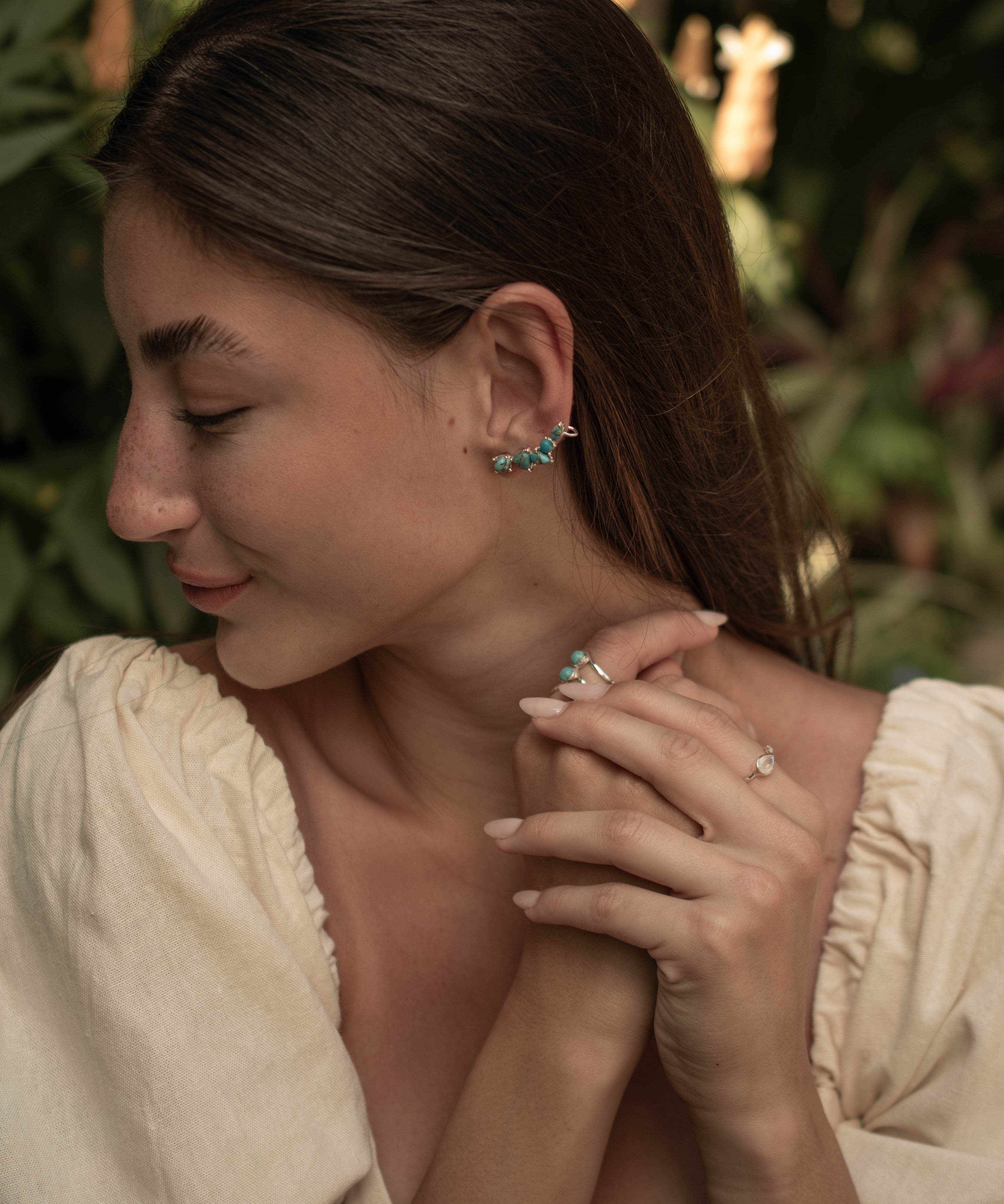 Woman wearing earrings and a ring with a blurred natural background