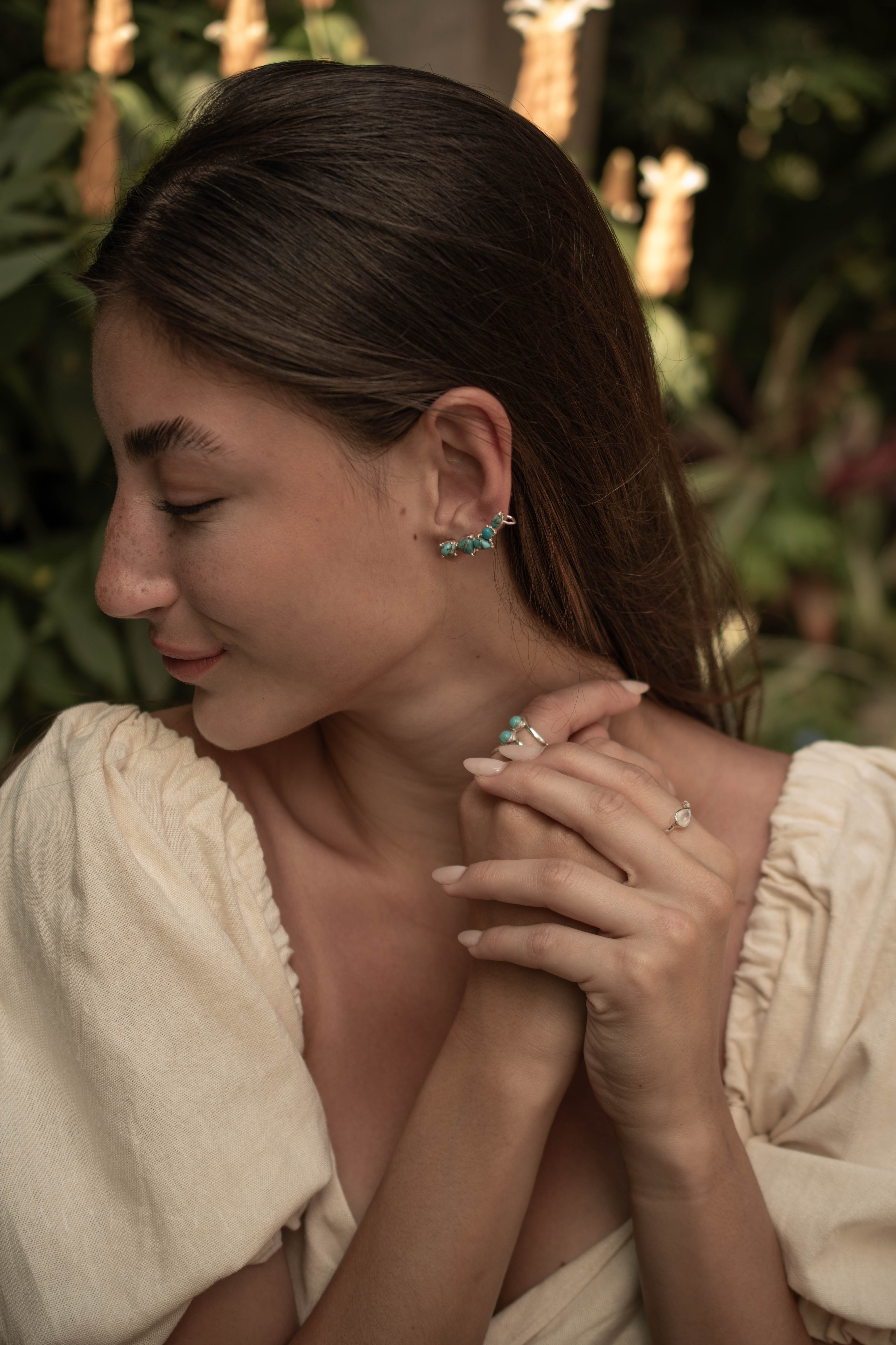 Woman wearing earrings and a ring with a blurred natural background