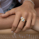 May include: Two gold rings with gemstone accents. One ring features a light blue, teardrop-shaped stone, while the other has a white, oval-shaped stone. A delicate gold bracelet with small, round beads is also visible. The rings and bracelet are displayed on a hand.
